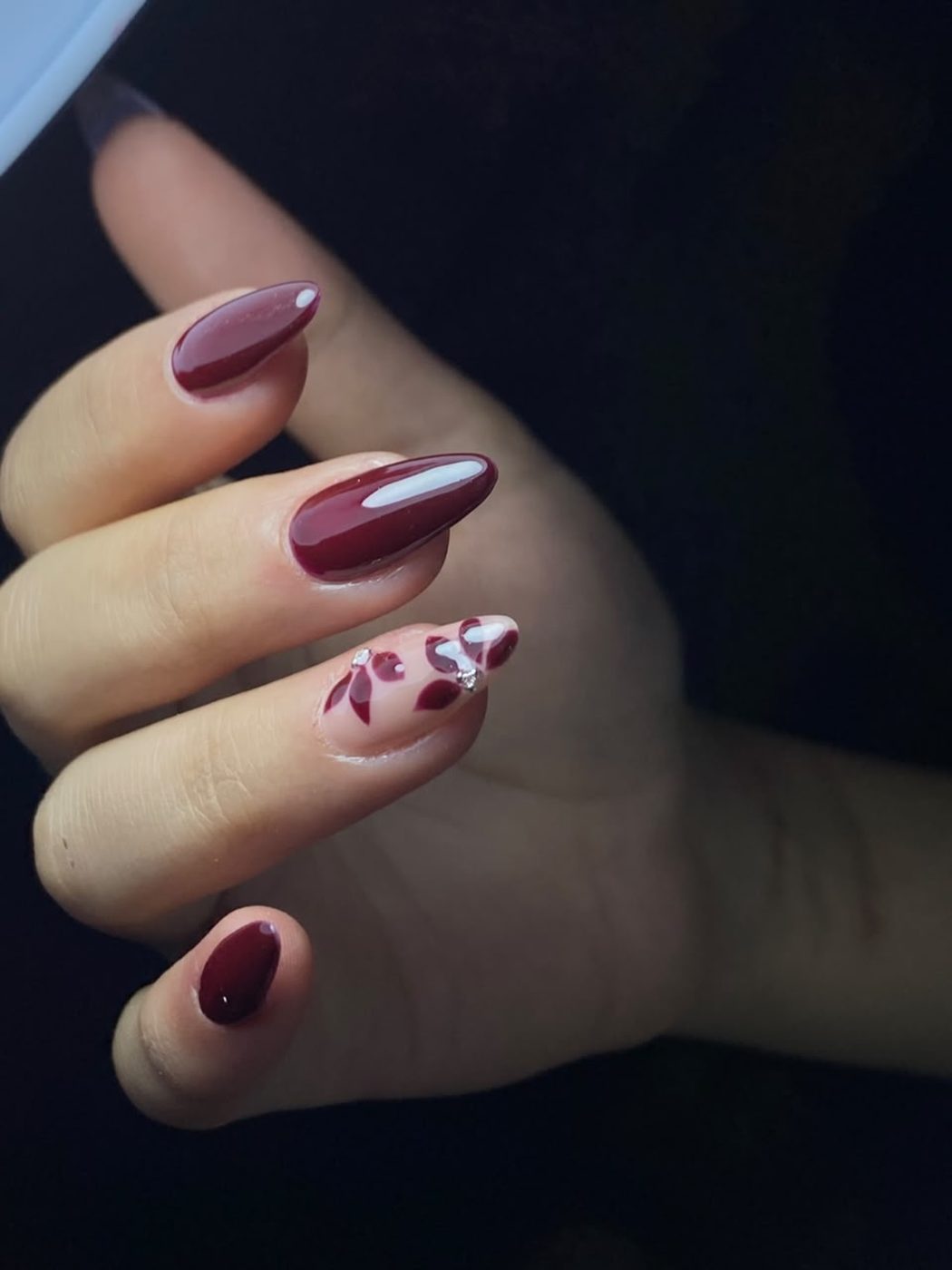 Burgundy gel nails with hand-painted floral accent and crystals